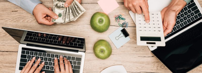 Top view of business people working with laptop, calculator and counting dollar banknotes at table
